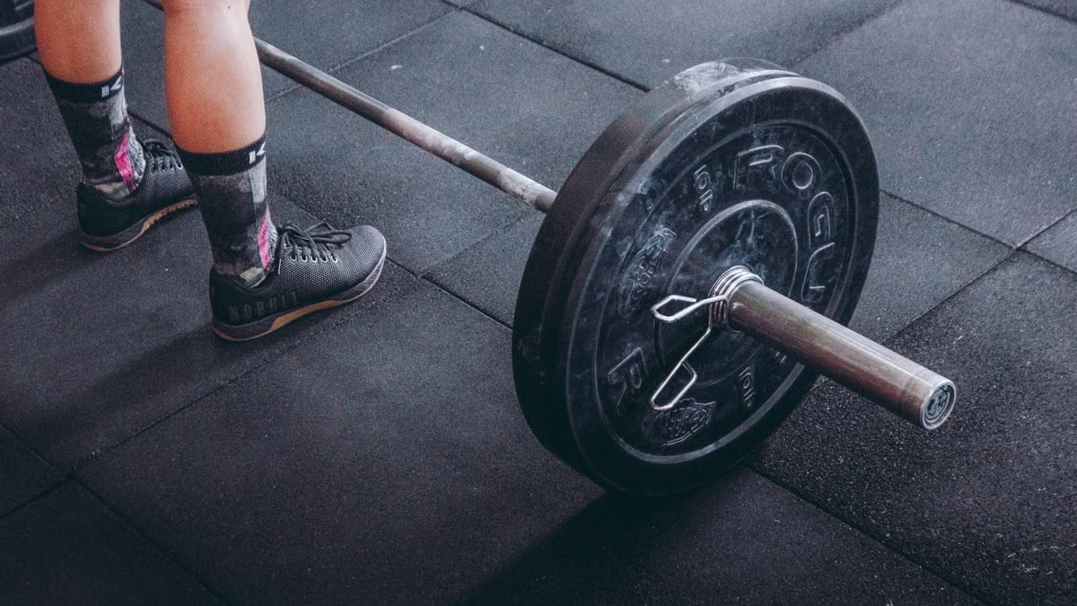Close-up of an athlete's legs beside a barbell, ready for weightlifting in a gym.